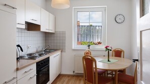A compact kitchen with white cabinets, a stove, and a dining area with a table and chairs.