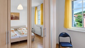 A bedroom with a bed, a chair, a window with curtains, a radiator, and a painting on the wall.