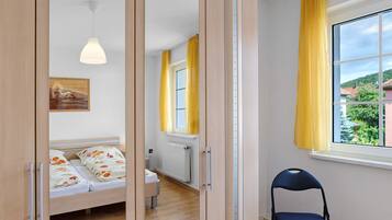 Ein Schlafzimmer mit Bett, Stuhl, einem Fenster mit Vorhängen, Heizkörper und einem Bild an der Wand.
