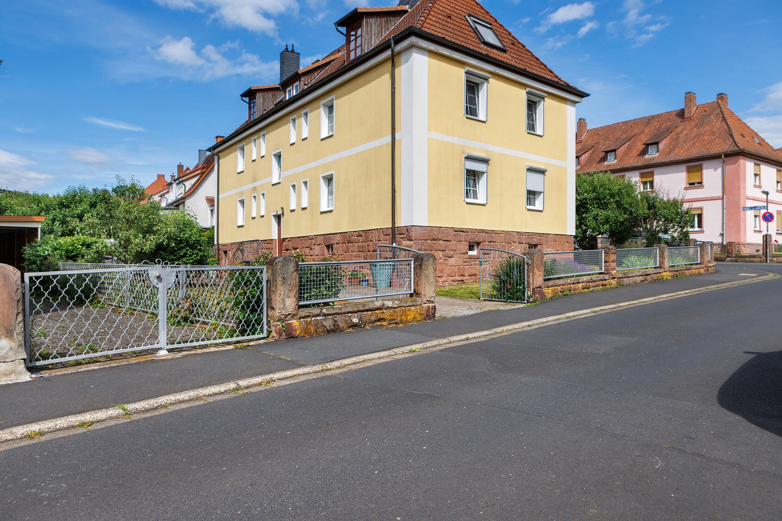 Ein gelbes Gebäude mit rotem Dach, einem verschlossenen Eingang und blauem Himmel.