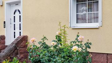 Ein Gebäude mit einer weißen Tür, einem Fenster mit weißem Rahmen und einem Rosenbusch davor.