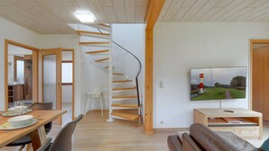 Un intérieur moderne avec un escalier en colimaçon, un coin repas, un salon doté d’un téléviseur et un plafond en bois.