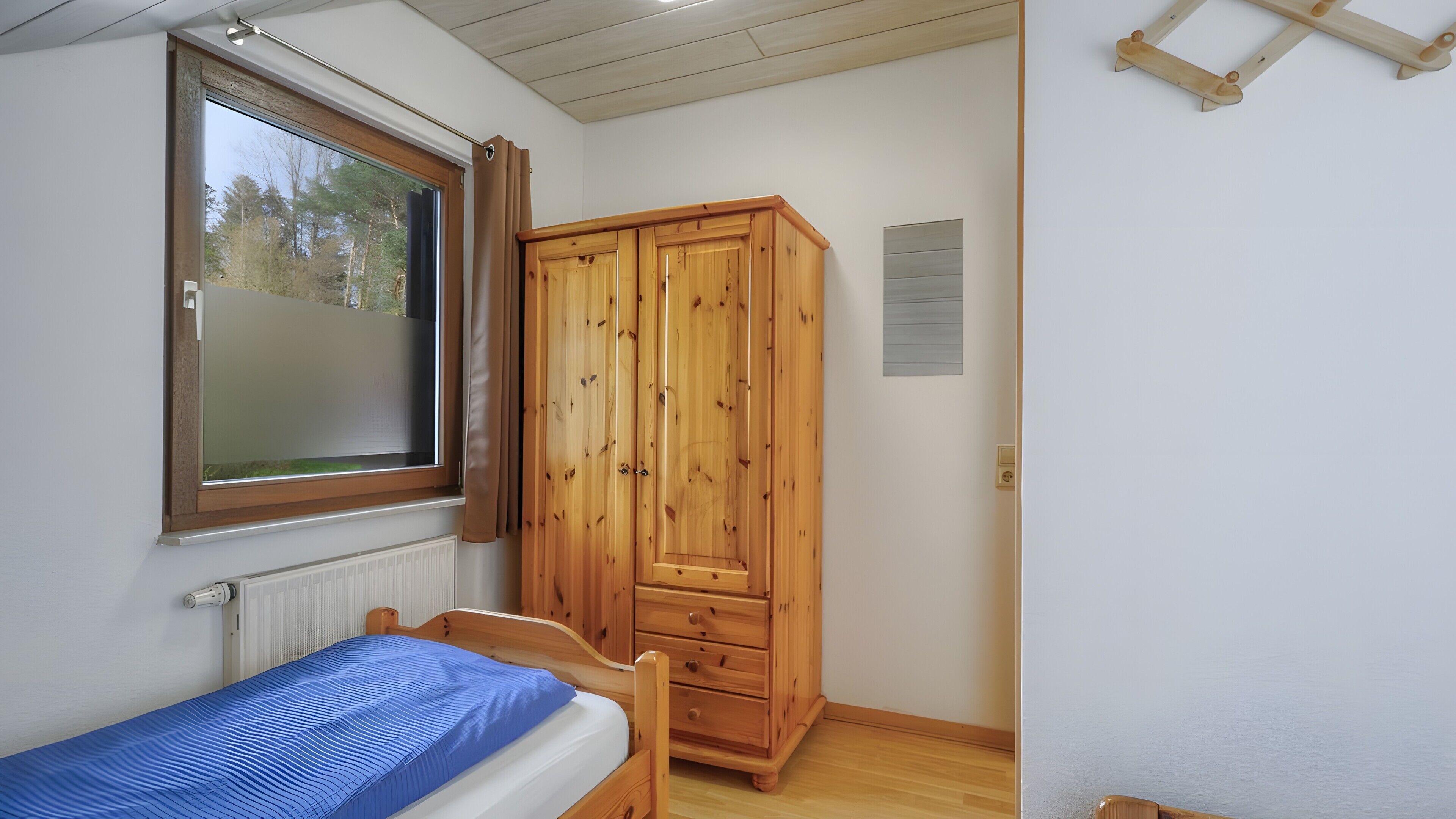 Een slaapkamer met een bed, een houten garderobe, een raam met gordijnen en een radiator.