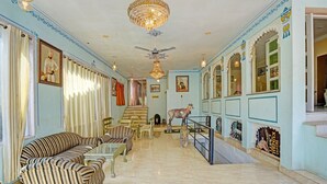 A hotel lobby with striped sofas, a chandelier, a ceiling fan, and a staircase leading to another level. - Classic Kumbhal Castle (Kumbhalgarh)