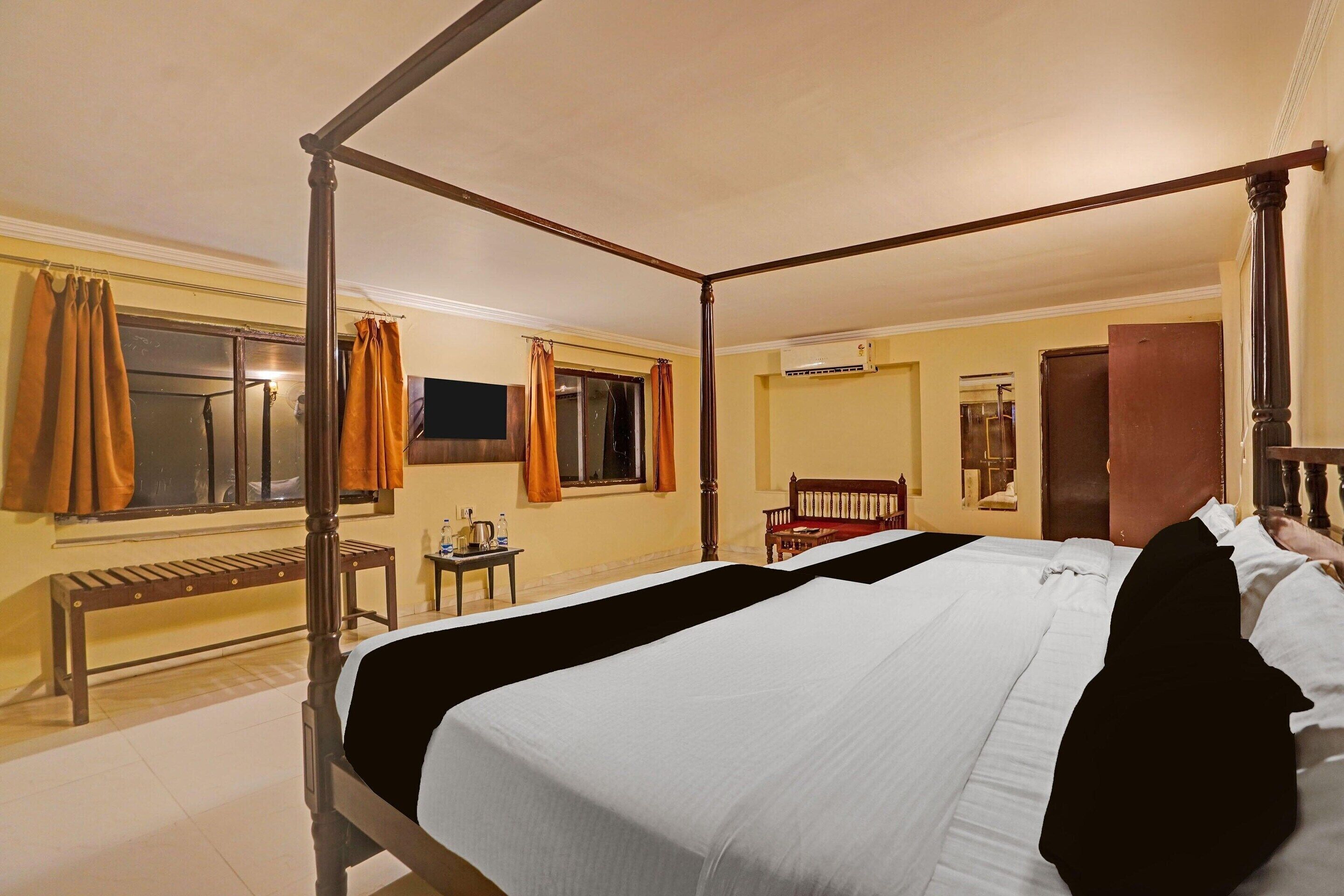 A four-poster bed with a wooden frame, a bench, a small table, and a mirror on the wall.