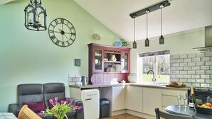 Un salon confortable avec un canapé, une table basse ornée d’un vase de fleurs, une cuisine équipée d’un évier et d’une cuisinière, et un coin repas avec une table et des chaises.