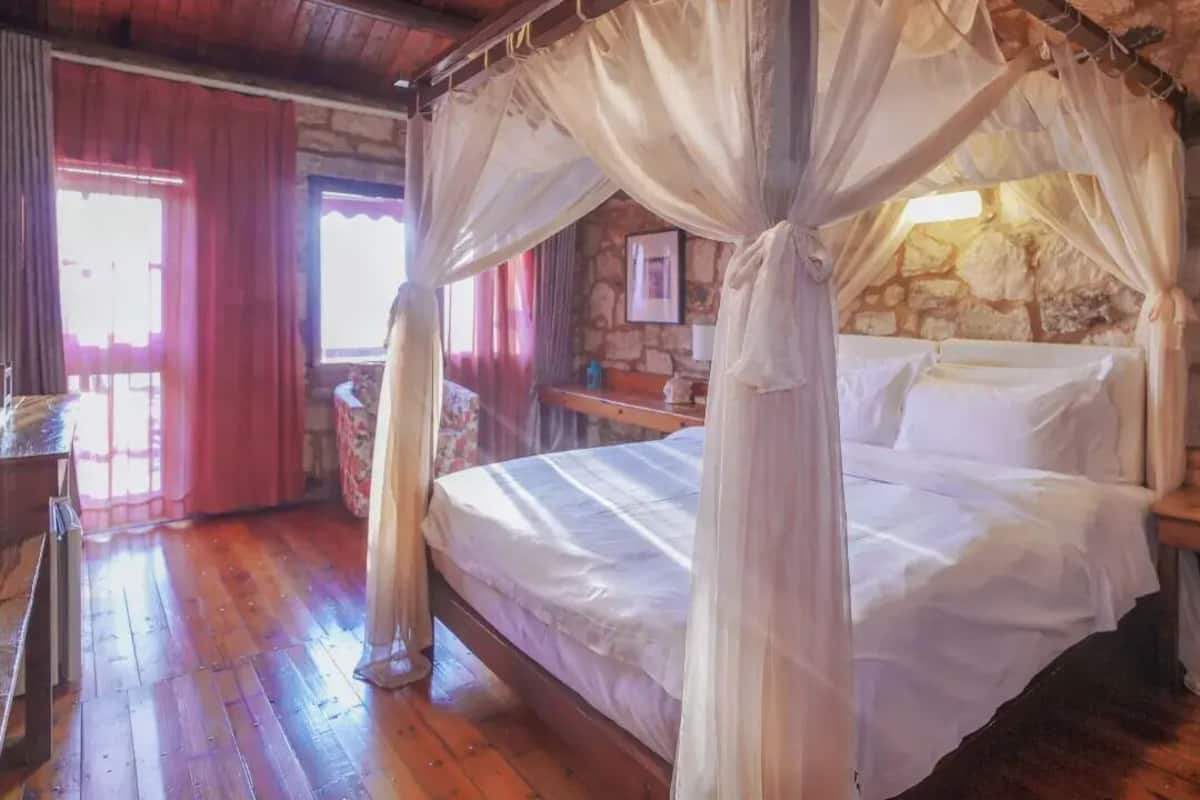 Une chambre dotée d’un lit à baldaquin, de murs en pierre, de planchers en bois, d’une table de chevet en bois et d’une fenêtre avec des rideaux.