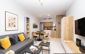 Una sala de estar moderna con un sofá gris, cojines amarillos, una mesita de centro y un televisor.
