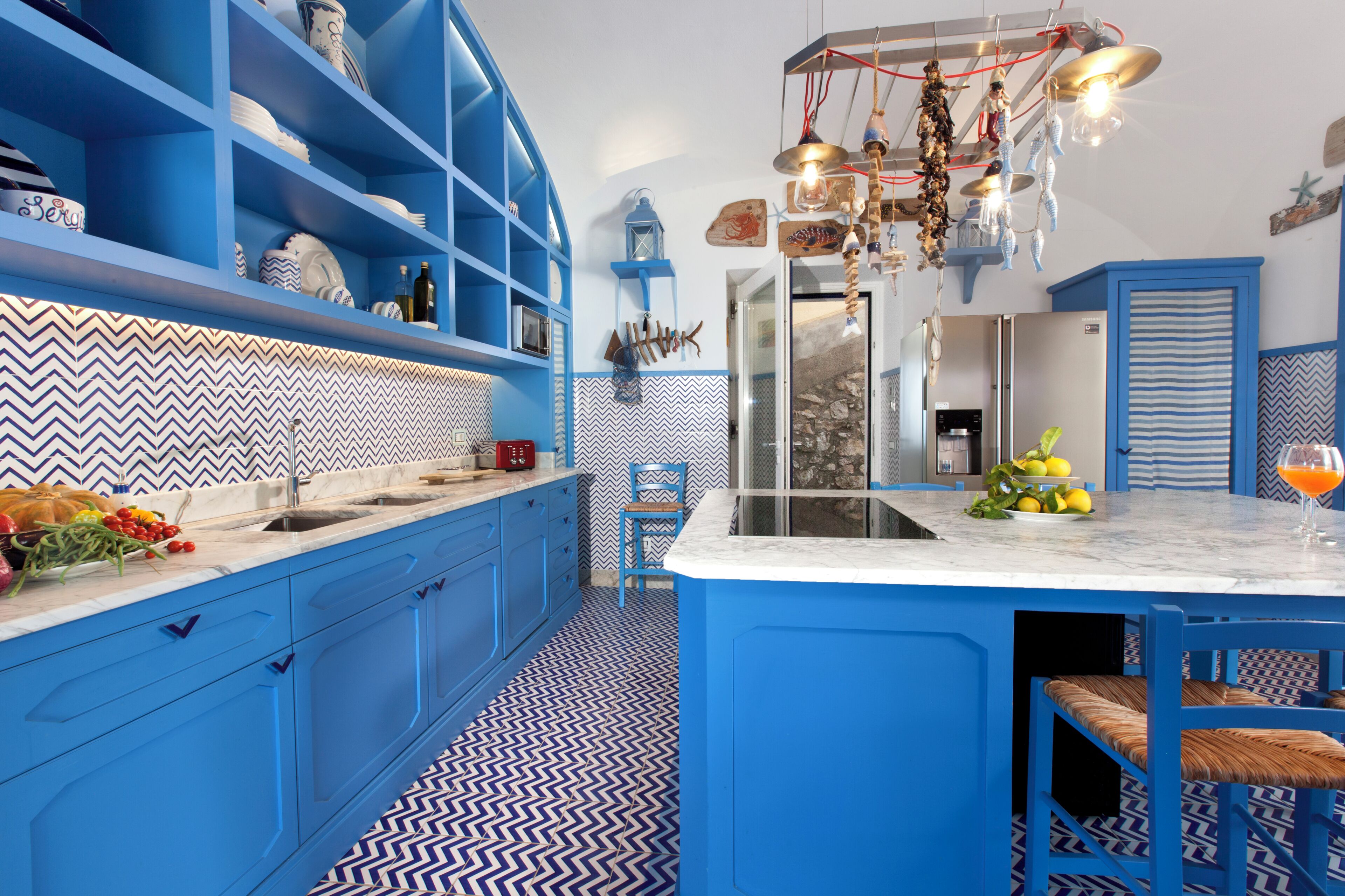 Une cuisine avec des armoires bleues, un îlot central en marbre et un sol à motifs.