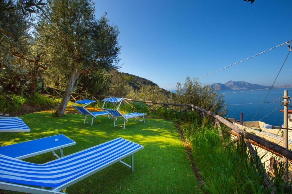 Uma área gramada com espreguiçadeiras listradas de azul e um cercado de madeira, com vista para um corpo d'água.