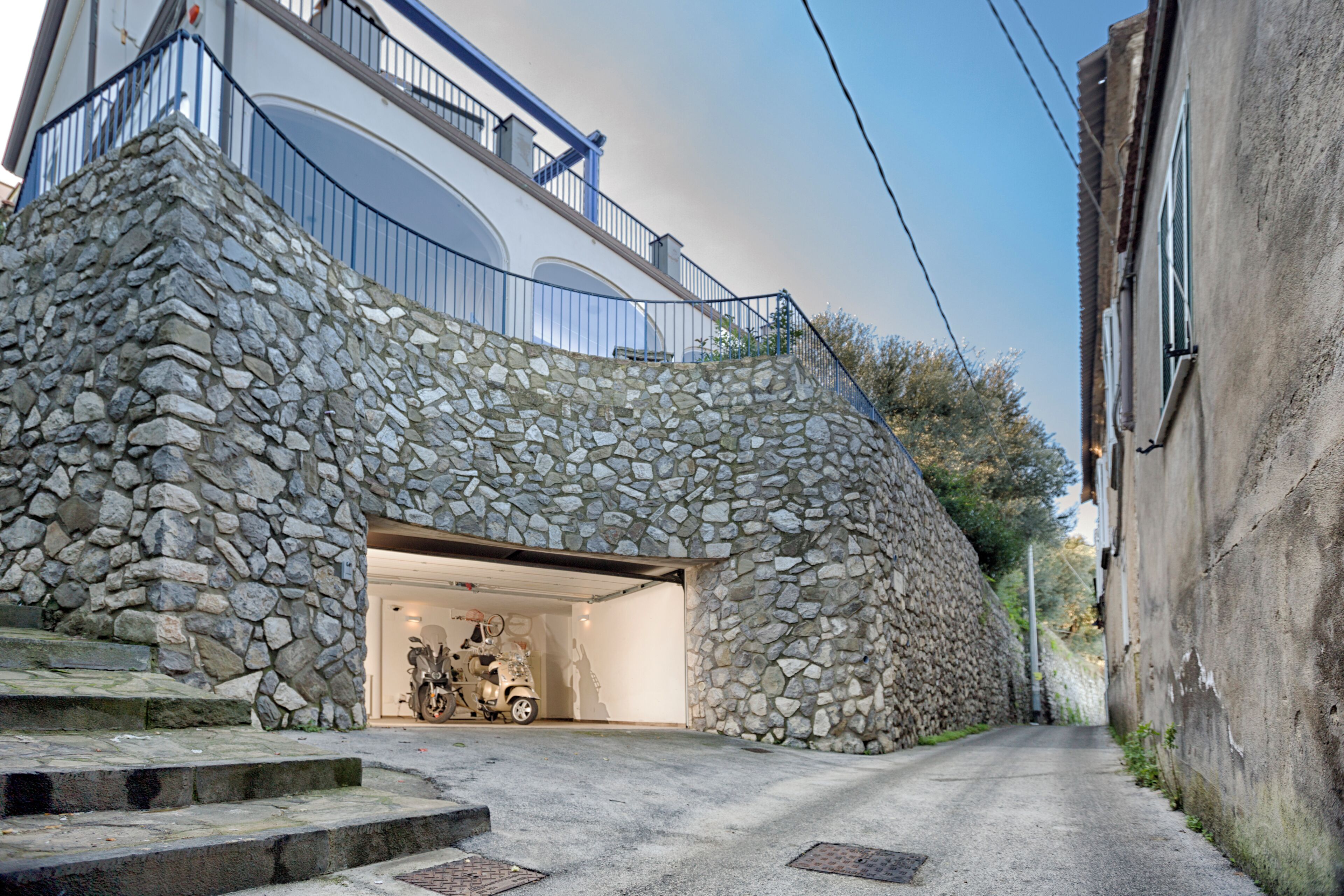 A stone-walled building with a garage entrance, steps leading up to the entrance, and a clear sky.