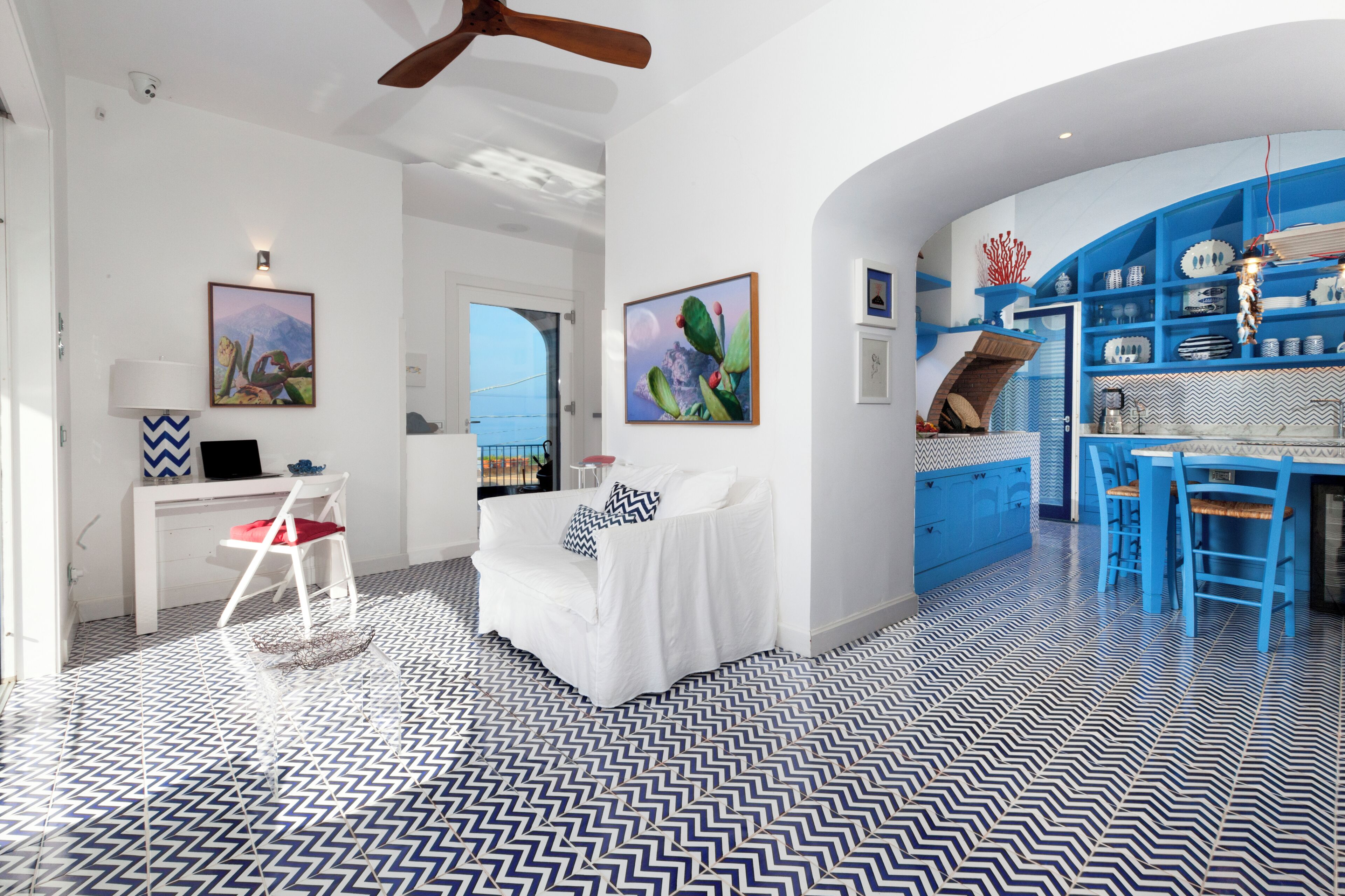 Een modern interieur met een witte bank, een zithoek met blauwe stoelen, en een keuken met blauwe kastjes.