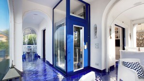 A spacious hallway with a blue accent wall, a glass door, and a white sofa with patterned cushions. - De Vivo Realty - Villa Blue Skyline (Marciano)