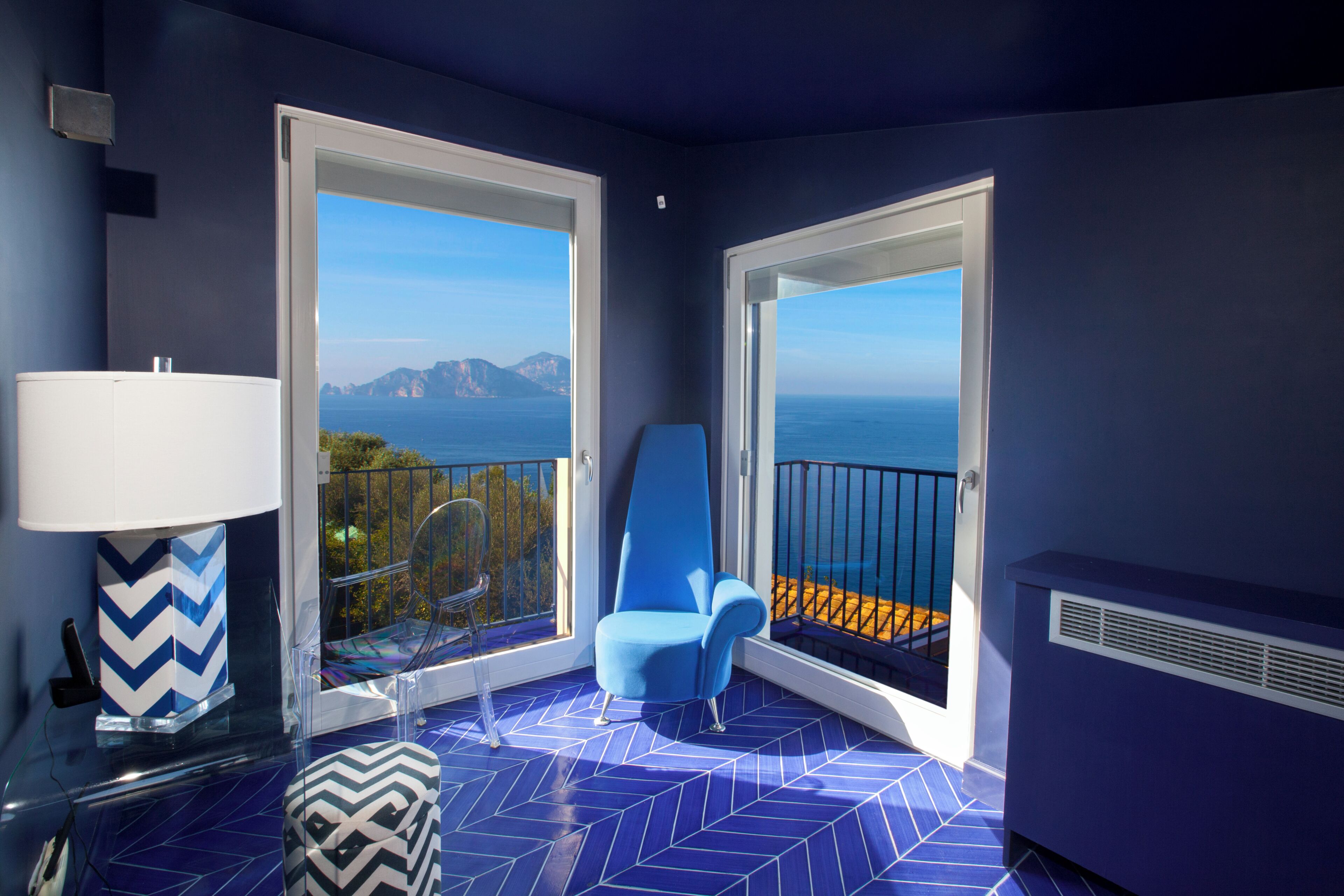 Uma varanda com vista para o mar, uma cadeira azul e um chão estampado.