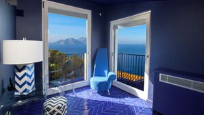 A balcony with a view of the sea, a blue chair, and a patterned floor. - De Vivo Realty - Villa Blue Skyline (Marciano)