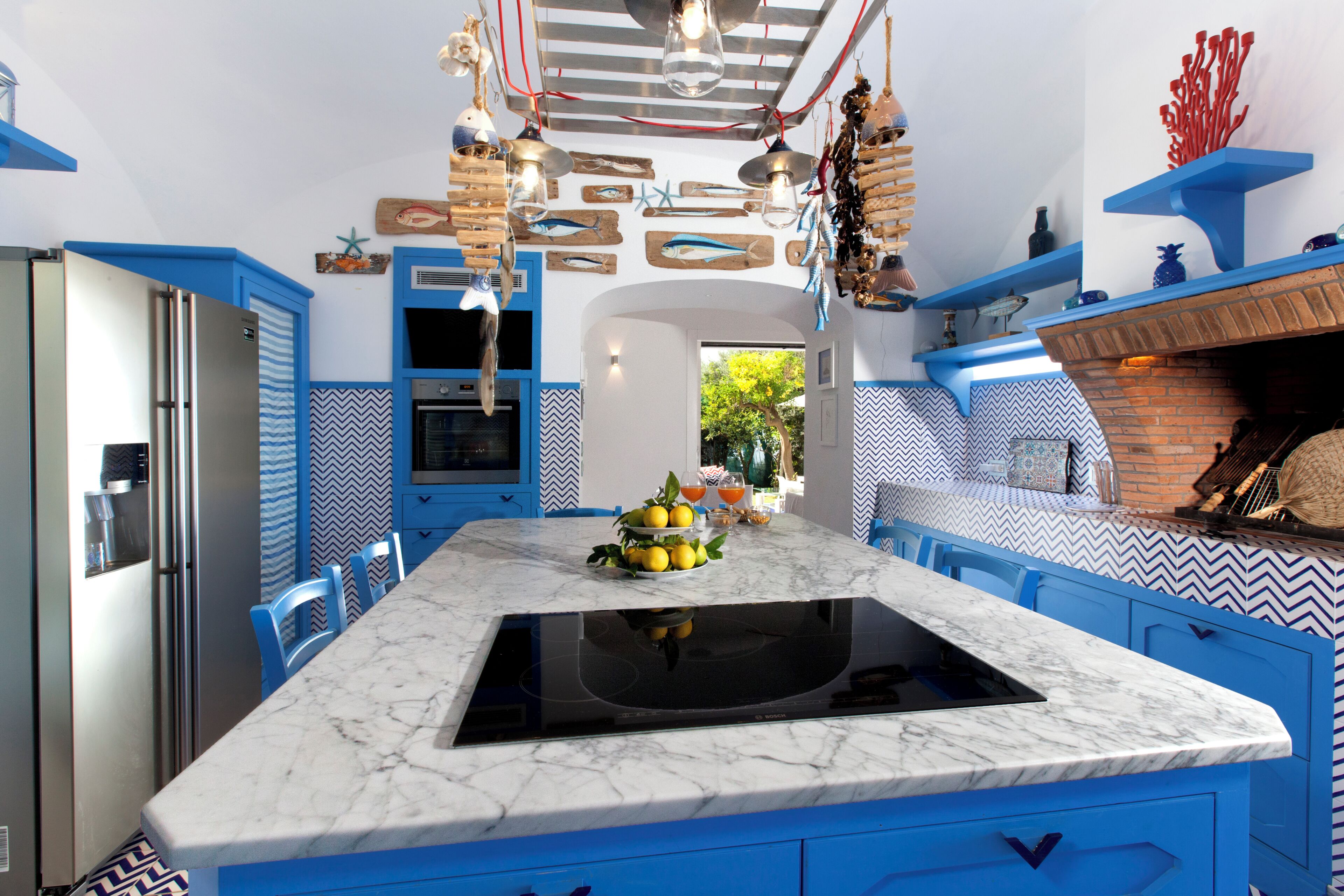 Une cuisine avec des meubles de rangement bleus, un plan de travail en marbre et une cuisinière intégrée.