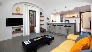 Ein modernes Wohnzimmer mit Flachbildfernseher, einem schwarzen Couchtisch, einem gelben Sofa und einer Küchenzeile mit Barhocker.