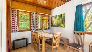 Una habitación con paneles de madera, una mesa, sillas, un radiador y una ventana con cortinas.