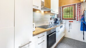 Una cocina compacta con armarios blancos, encimera de madera, horno empotrado y una ventana con cortinas de cuadros rojos y blancos.