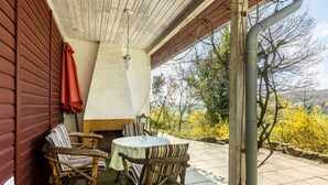 Un porche cubierto con una mesa y sillas, un farol colgante y vistas a árboles y colinas.