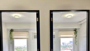 Ein Hotelzimmer spiegelt sich im Spiegel, mit einem Bett, Kissen, einem Holzkopfende, einem Fenster mit Jalousien und Blick auf die Stadt.
