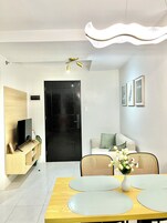 Una sala moderna con televisor de pantalla plana, una puerta negra, un sofá, una mesa de comedor con individuales y una lámpara de techo.