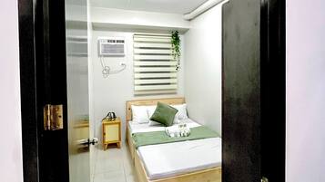 A bedroom with a bed, a bedside table, a wall-mounted air conditioner, and a window with blinds.