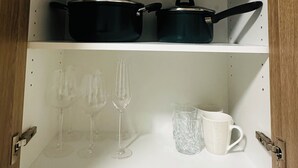 A kitchen cabinet with two black pots on the top shelf and wine glasses and a mug on the bottom shelf. - Modern Studio Sydney (108) - 2 km to Sydney University (Stanmore)