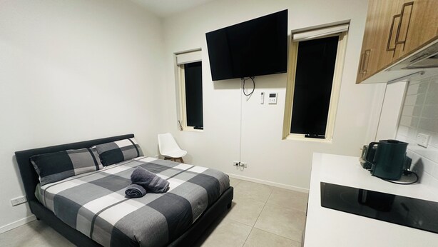 A bedroom with a bed, a TV mounted on the wall, a window, and a kitchenette area. - Modern Studio Sydney (108) - 2 km to Sydney University (Stanmore)