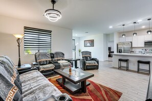 Sala moderna com sofá, mesa de centro e área de cozinha com geladeira e banquetas.