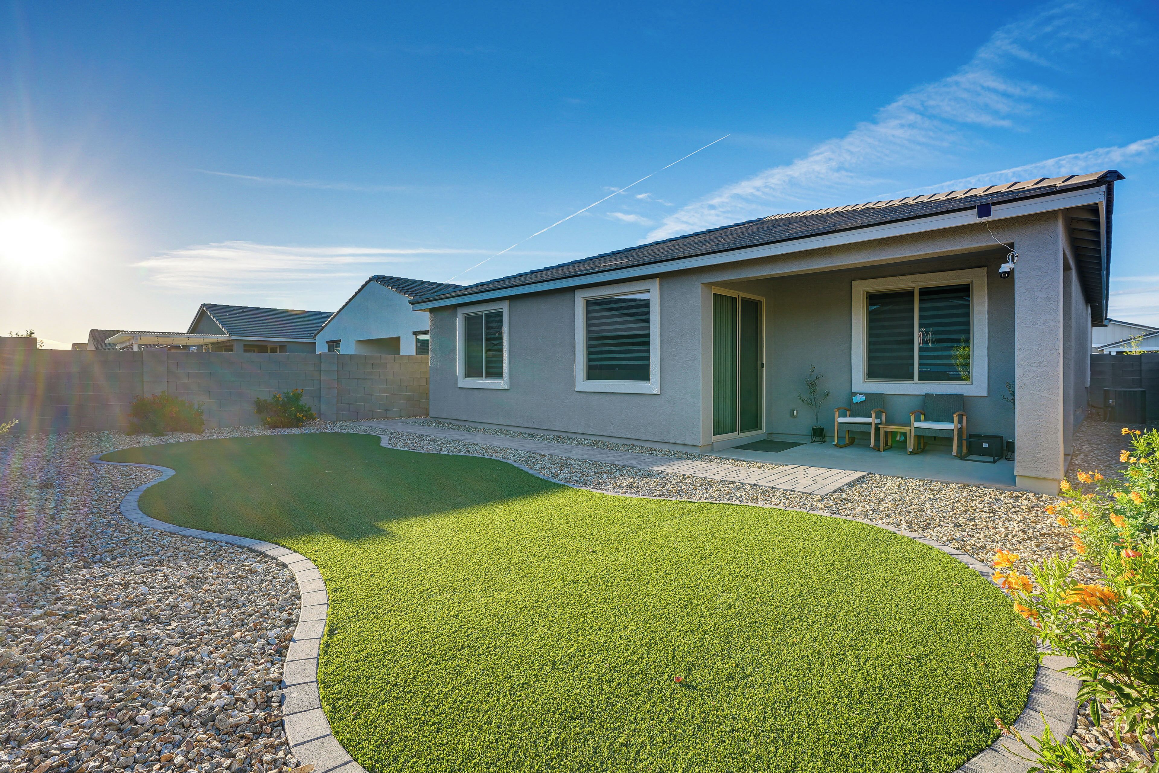 Une maison moderne avec une pelouse bien entretenue, une terrasse dotée de mobilier d’extérieur et un ciel dégagé.