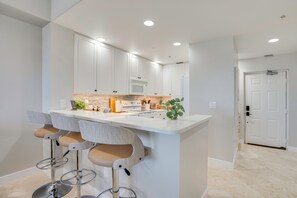 Une cuisine moderne avec des meubles blancs, un îlot central doté de tabourets et un four encastré.