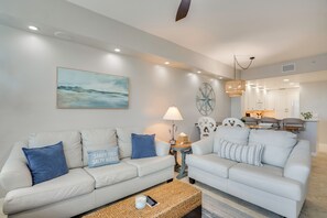 Un salon avec deux canapés blancs, une table basse, une lampe et un tableau accroché au mur.