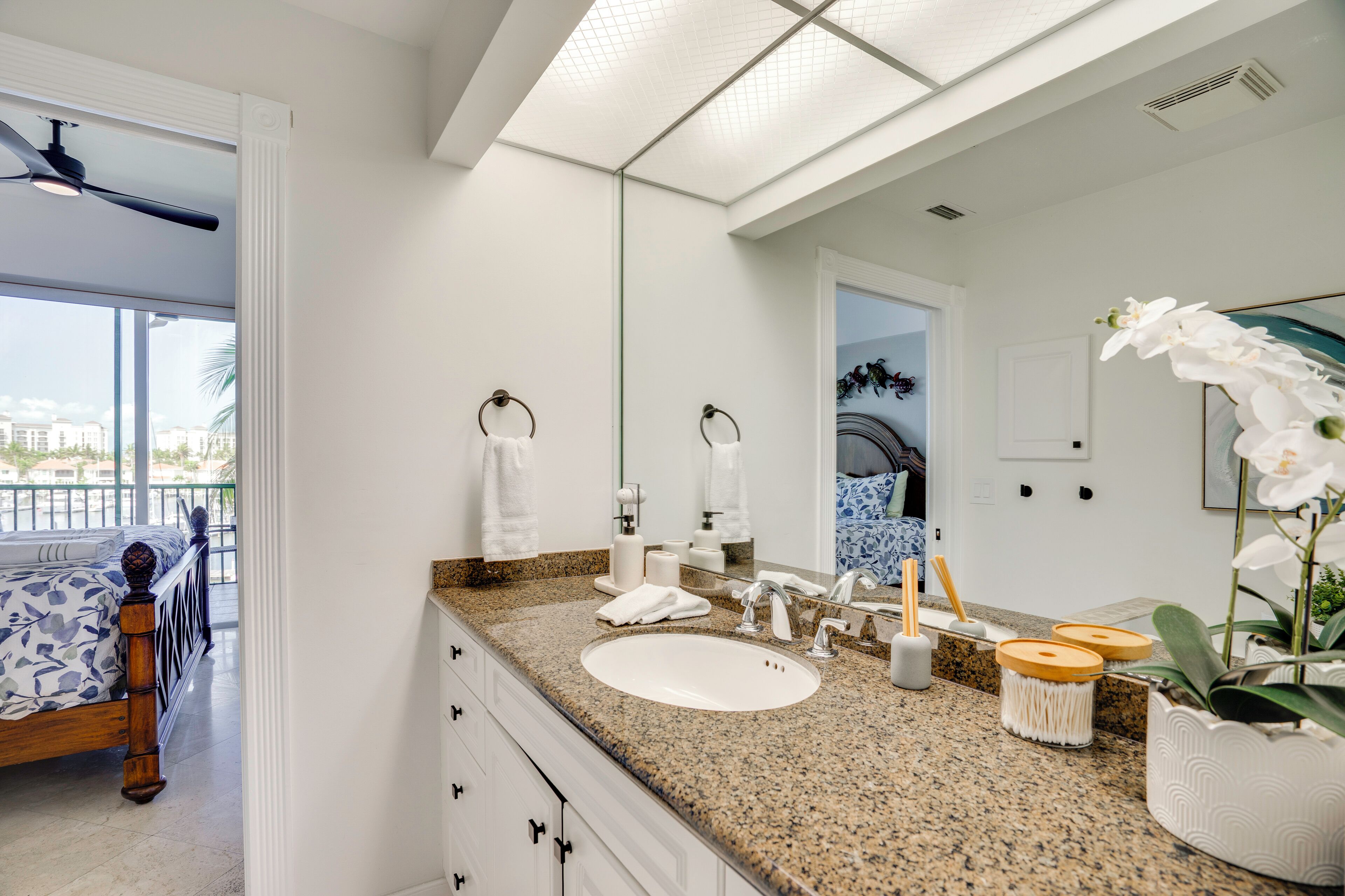 A modern bathroom with a large mirror, white sink, and a ceiling fan.