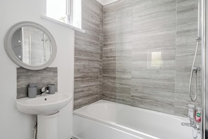Une salle de bain avec un lavabo blanc, un miroir rond et une douche dotée d’une porte en verre.