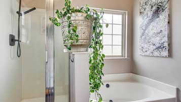 A bathroom with a glass-enclosed shower, a freestanding bathtub, and a potted plant.