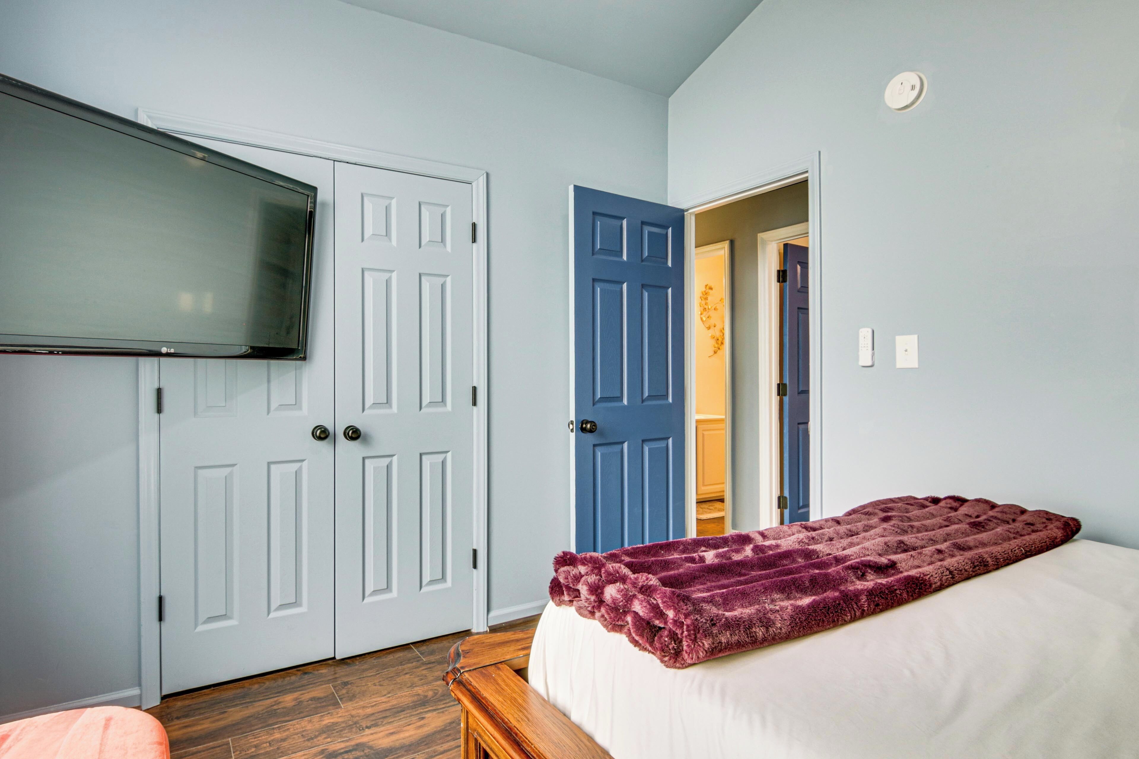 A bedroom with a bed, a TV mounted on the wall, and two doors.