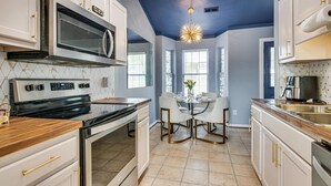 Una cocina moderna con armarios blancos, un microondas integrado y un comedor con mesa y sillas de vidrio.