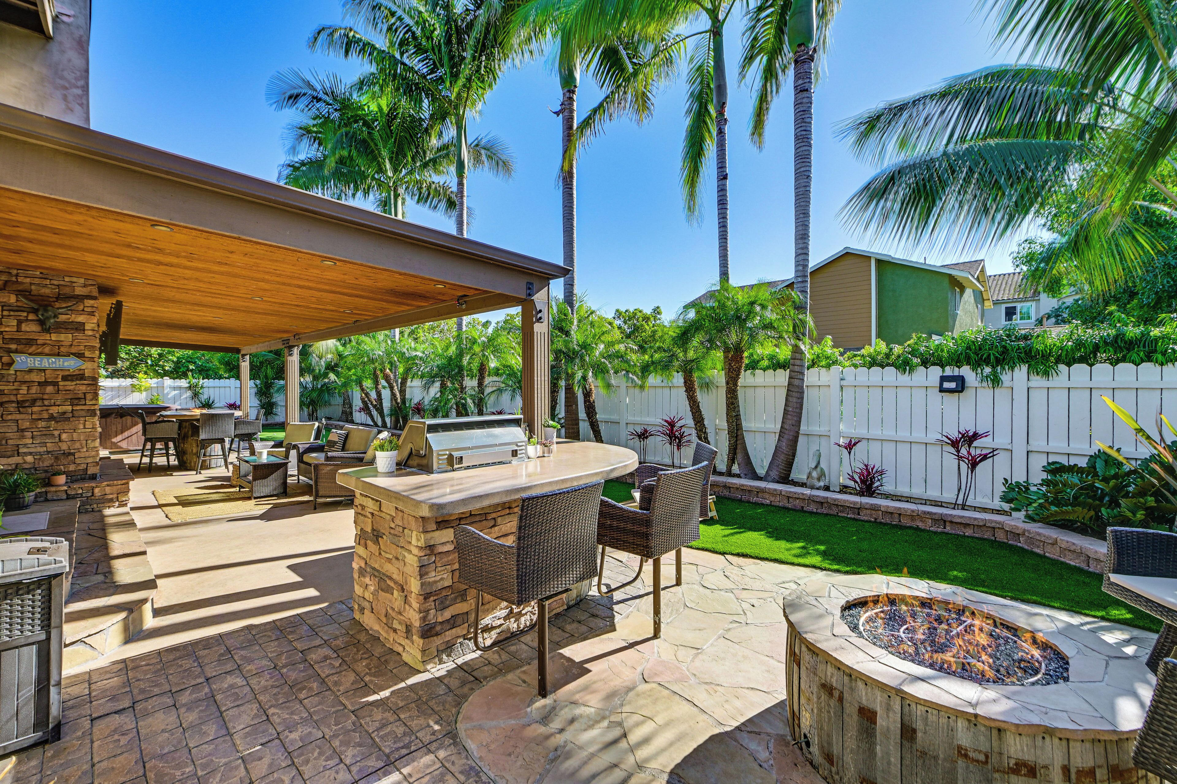 An outdoor patio with a stone barbecue area, wicker furniture, and a fire pit.