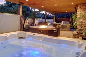 A hot tub with a fire feature, outdoor seating, and a stone wall. - Walk to Lagoon! Luxe Coastal Escape w/ Pool Table (Carlsbad)