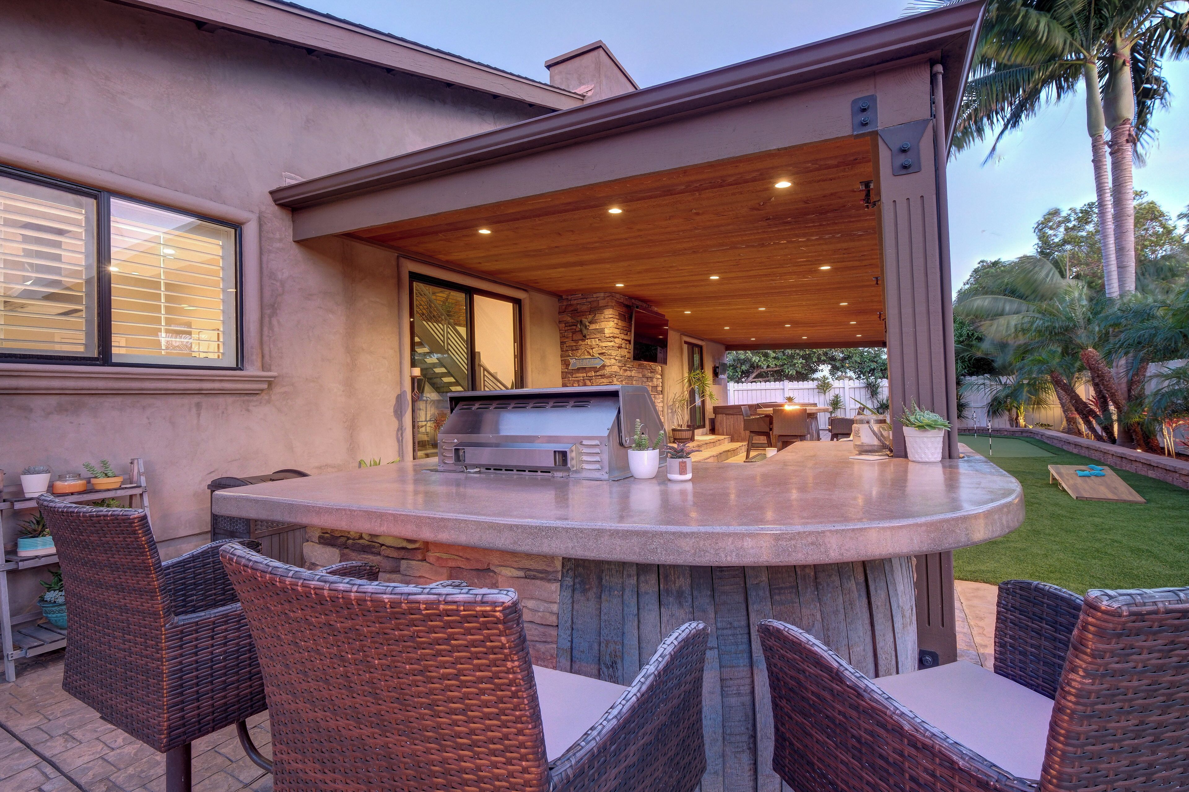 Une cuisine extérieure équipée d'un barbecue, d'un espace repas avec des chaises en osier et d'un mur décoratif en pierre.
