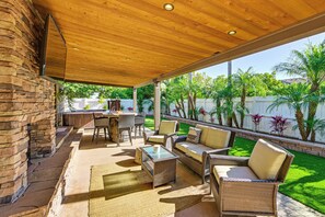 A covered patio with wicker furniture, a glass table, and a stone wall. - Walk to Lagoon! Luxe Coastal Escape w/ Pool Table (Carlsbad)