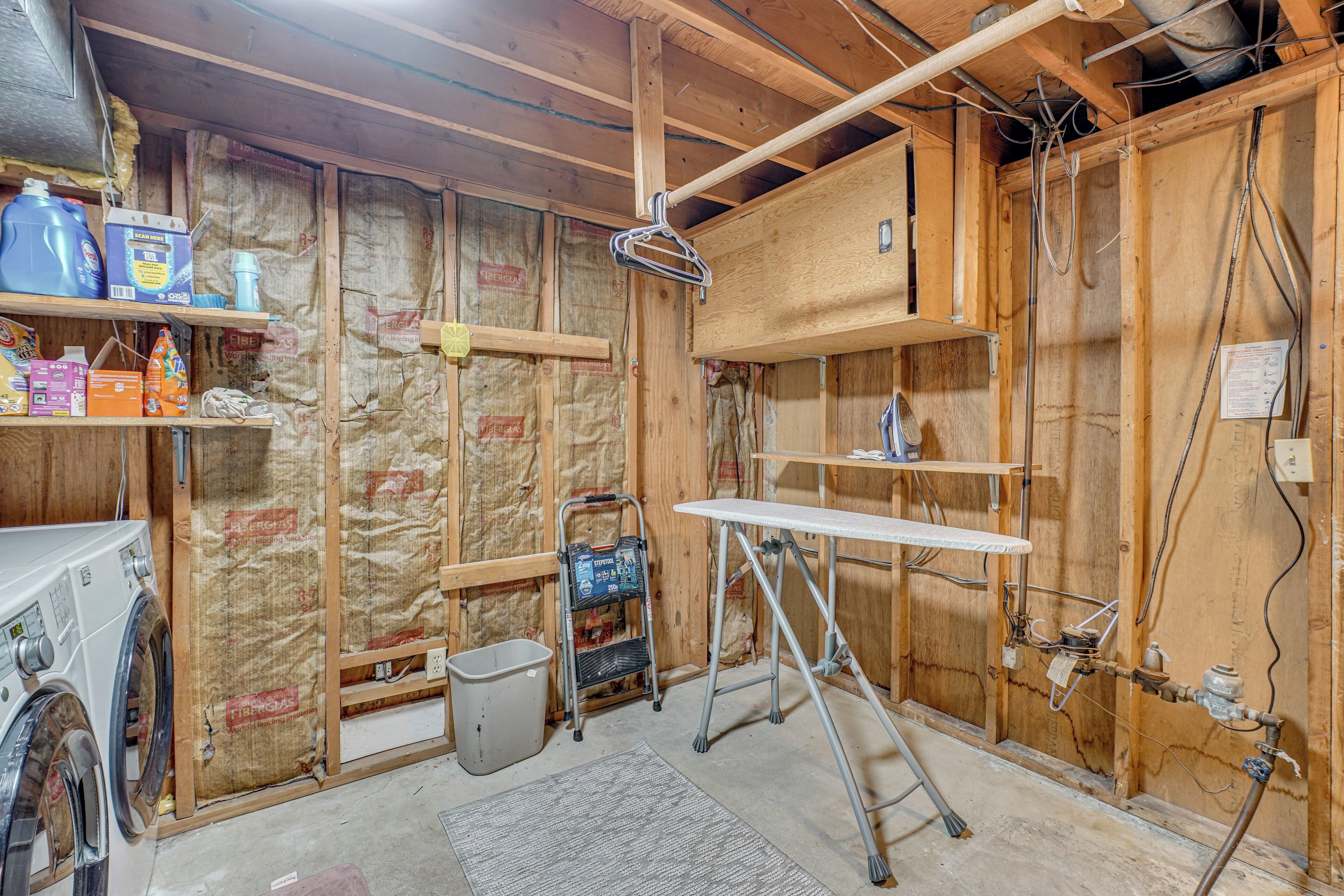 A room under construction with exposed wooden walls, a washing machine, a utility cart, and a workbench.