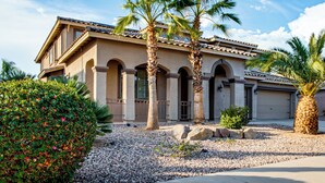 A two-story house with a tiled roof, arched columns, and a gravel driveway. - Swim-up Bar & Games! Ultimate Goodyear Group Stay (Goodyear)