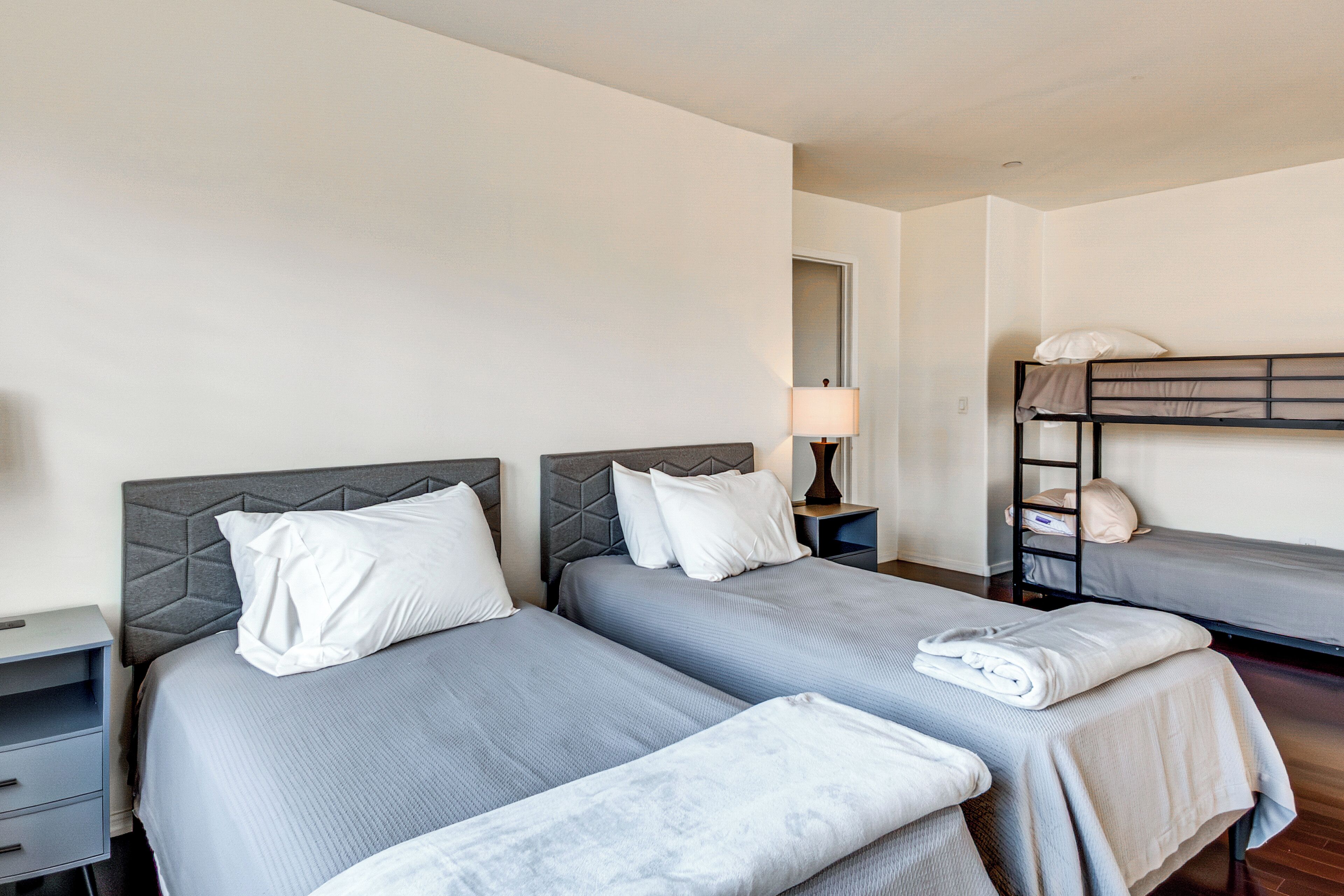 Une chambre d’hôtel avec deux lits simples, une table de chevet, une lampe et un lit superposé.