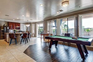 A spacious living area with a pool table, a kitchen with a bar, and large windows offering a view of the outdoors. - Swim-up Bar & Games! Ultimate Goodyear Group Stay (Goodyear)