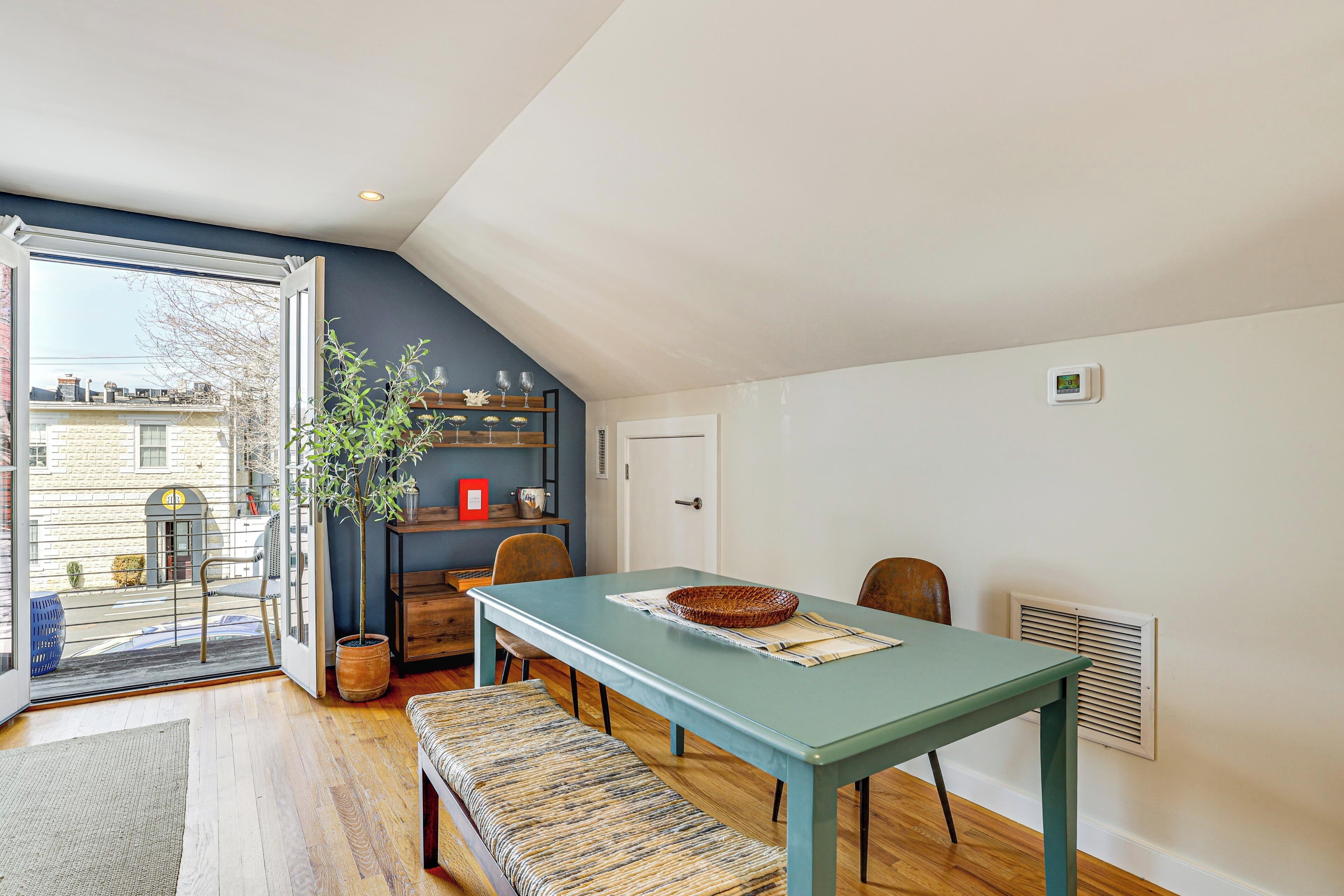 Een eetruimte met een tafel, stoelen, een bankje, een potplant en uitzicht door een glazen deur.