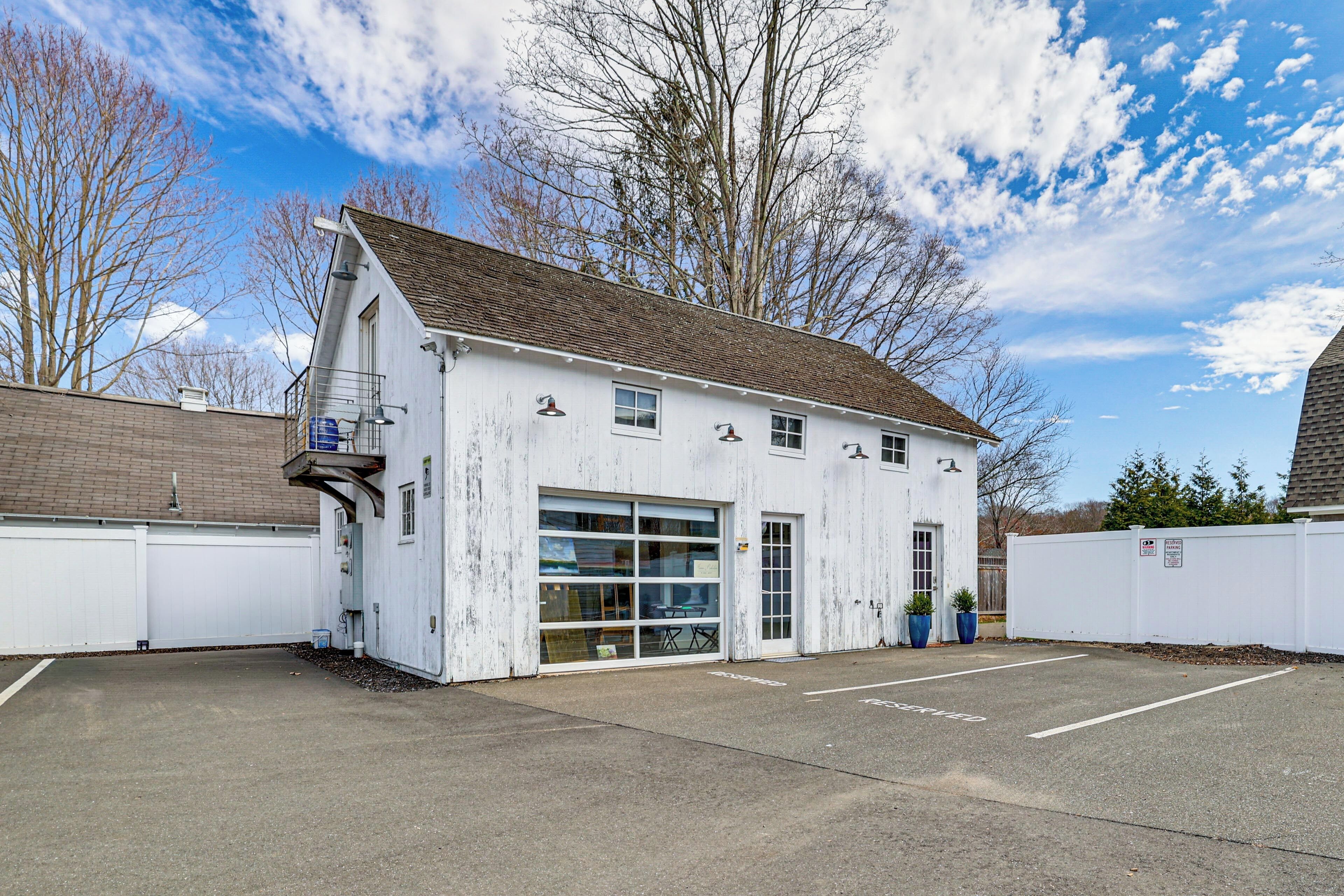 Un bâtiment blanc doté de grandes fenêtres et d’une porte de garage, entouré d’un parking et d’une clôture.