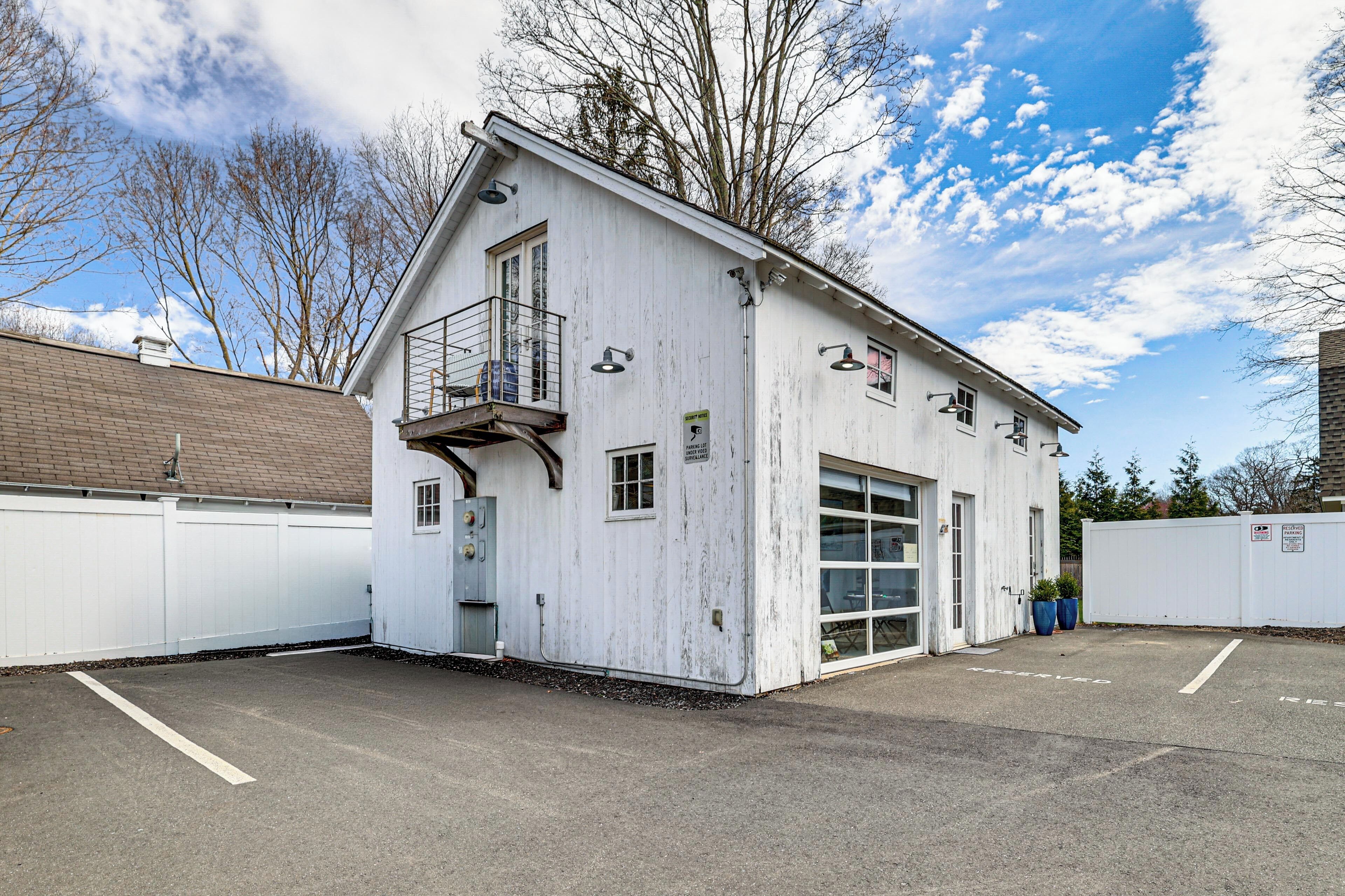 A white building with a garage door, a small balcony, and a parking lot.