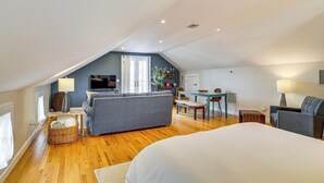 Une chambre spacieuse située dans les combles, avec un grand lit, un canapé gris, un coin repas et un téléviseur.